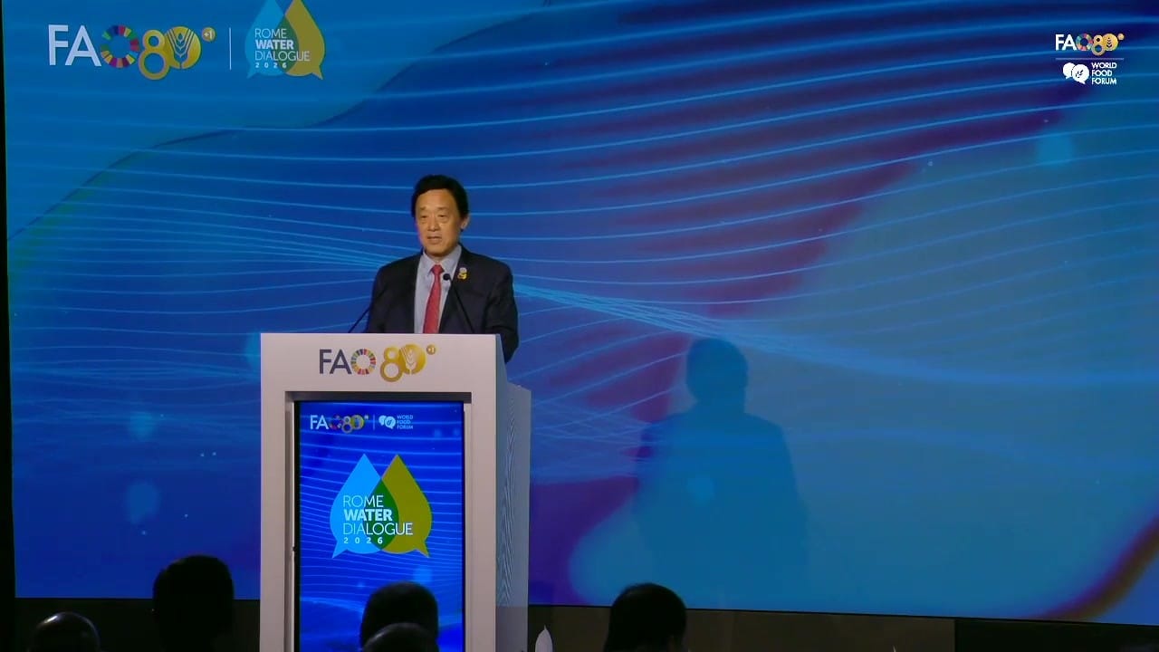 QU Dongyu at the lectern of FAO's Plenary Hall, seen from the back of the hall, with the Rome Water Dialogue 2026 logo on the screen